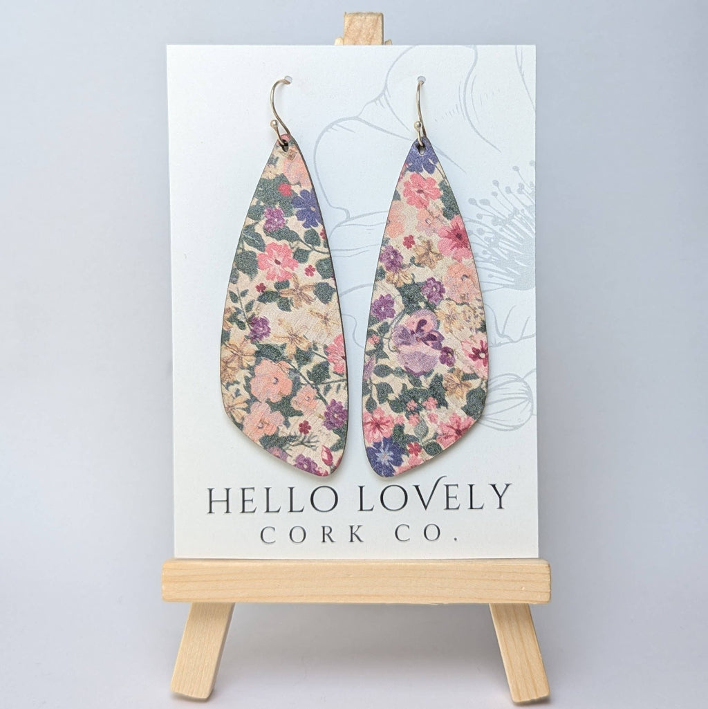 A pair of floral patterned pink pansies cork earrings displayed on a white card with the text 'Hello Lovely Cork Co.'
