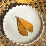 Pair of yellow leaf-shaped earrings on a white plate with a woven mat background